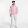 Hoodie rose clair pour homme, modèle "Rose Sprint" signé Tourismo Clothing. Sweat à capuche sans cordon, poche kangourou classique, logo noir "TOURISMO" et damier brodé sur la poitrine gauche. Le modèle pose de face, mains dans les poches, pantalon blanc, sneakers Nike blanches, ambiance sobre sur fond blanc. Coupe droite et minimaliste, esprit racing lifestyle revisité en version douce et urbaine.