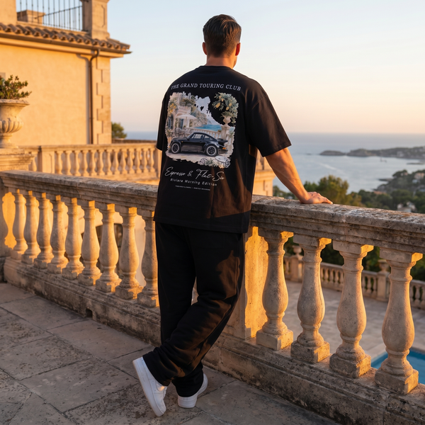 Homme portant le t-shirt noir Grand Touring Club 911 Turbo sur une terrasse en pierre face à la mer au coucher du soleil