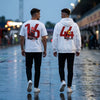 Deux mannequins de dos marchant dans une voie de paddock détrempée au crépuscule, en t-shirt Charles Leclerc 16 et sweat Lewis Hamilton 44