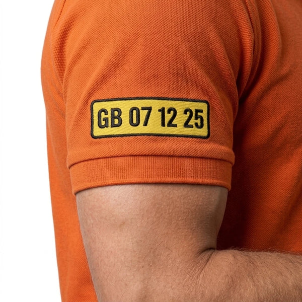 Plaque GB 07 12 25 brodée sur la manche du polo orange Lando Norris, vue portée