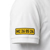 Gros plan sur la plaque MC 26 05 24 brodée sur la manche du polo blanc