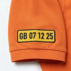 Gros plan sur la plaque GB 07 12 25 brodée sur la manche du polo orange