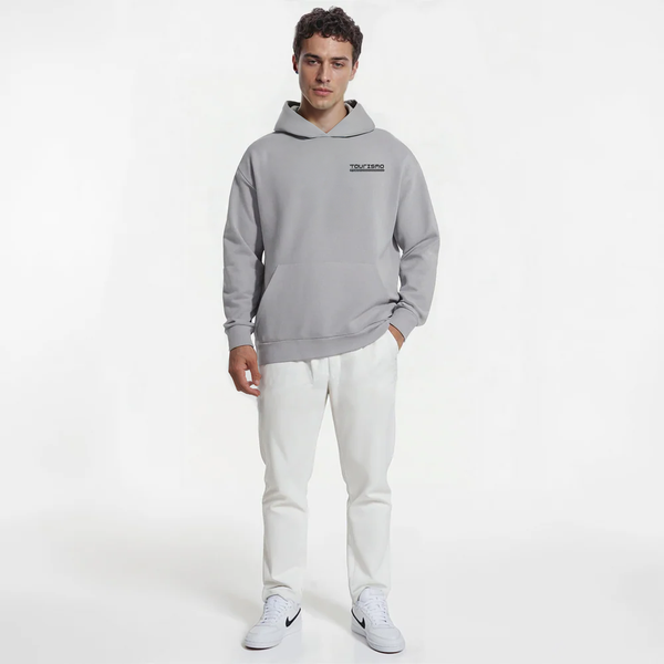 Homme en sweat gris clair TOURISMO, pantalon blanc et sneakers Nike sur fond blanc