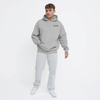 Homme portant un hoodie gris clair TOURISMO avec un jean clair et des sneakers, fond blanc