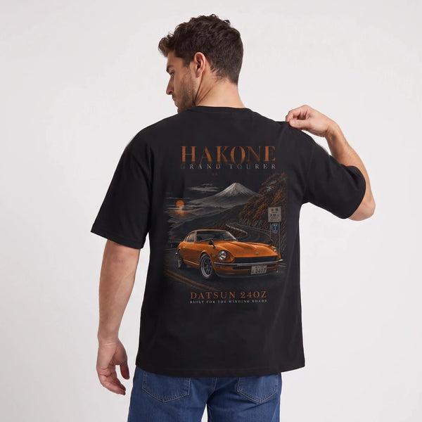 T-shirt Datsun 240Z noir, sportive orange sur une route de montagne vue de dos